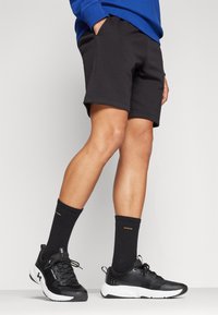 Pantaloni sportivi neri con vita elasticizzata, abbinati a calze nere lunghe fino al ginocchio e scarpe da ginnastica nere con accenti bianchi.