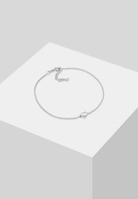 Silverarmband med en tunn, texturerad kedja och en slät hjärtformad berlock. Har en spänne och en justerbar längd på kedjan.