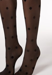 Schwarz gemusterte Strumpfhosen aus semi-opakem Material mit großen schwarzen Pünktchen, glatter Textur und angepasstem Design.