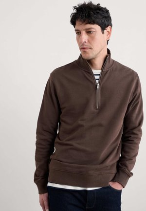 Bruine sweatshirt met rits en lange mouwen, gemaakt van zachte stof, met een ribbelzoom. Draagt over een gestreept shirt, met een ontspannen pasvorm.