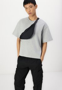 Grå kortærmet T-shirt parret med sorte cargo-bukser og en sort crossover-taske, der har en glat tekstur og justerbar strap.