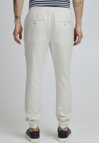 Joggers ligeros de lino color crema con una cinturilla elástica, tobillos ajustados y dos bolsillos traseros con cierres de botón.