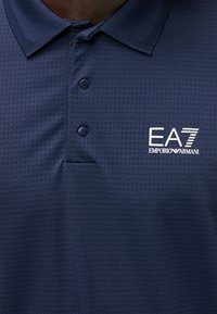 Polo bleu marine avec carrés texturés, deux boutons et logo blanc EA7 Emporio Armani sur la poitrine.