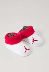Chaussettes blanches pour bébé avec une bordure rouge, ornées de logos Jumpman rouges sur le côté extérieur. Fabriquées dans un tissu doux et extensible.