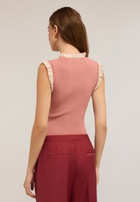 Top senza maniche in tessuto a coste rosa polveroso con un colletto crema arricciato. Abbinato a pantaloni bordeaux a vita alta con tasche posteriori.