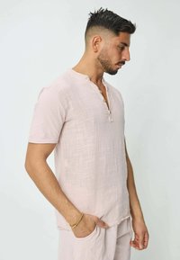 Chemise rose pâle à manches courtes avec une finition texturée, col rond et trois boutons à l'avant. Coupe décontractée avec un ourlet subtil.