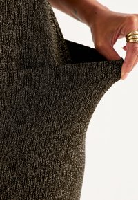 Svart stickad tyg med en subtil lyster, med en ribbad textur. En hand drar i materialet och visar en elastisk midja.