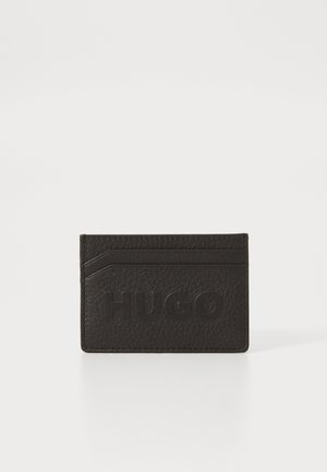 Porta-cartões de couro preto texturizado com o logótipo "HUGO" em relevo, apresentando um design de ranhura para cartões angulado e uma forma minimalista.