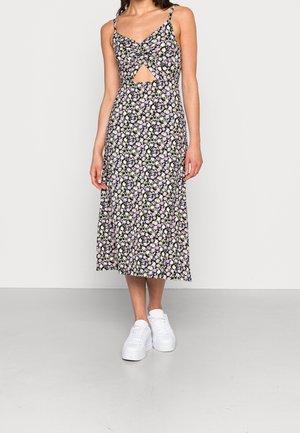 Blommig midiklänning i svart med lila och gula blommor, med en tvistet front och utskurna detaljer. Matchas med vita sneakers.