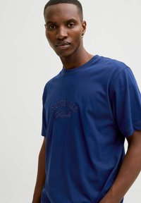 Camiseta de algodón azul marino con mangas cortas, cuello redondo y logo en relieve "ORIGINALS" en el pecho. Textura suave, corte relajado.