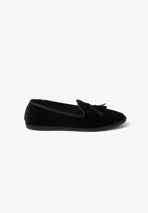 Black velvet flat loafer with rounded toe and tassel detailing on white background, viewed from the side.