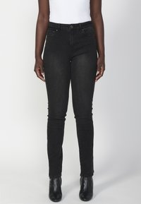 Jeans de mezclilla negra ajustados con cintura alta, bolsillos delanteros y cierre de botón. Combinados con botas hasta el tobillo, mostrando un ajuste elegante.