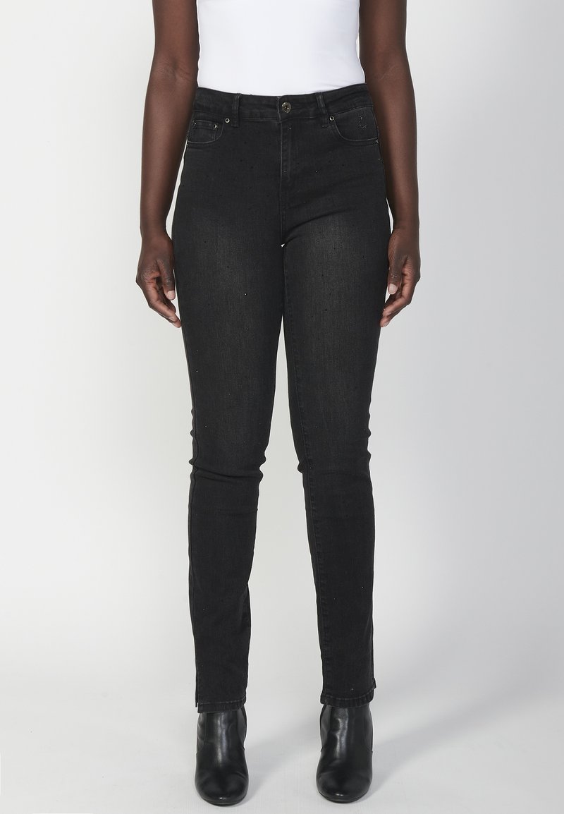 Jeans de mezclilla negra ajustados con cintura alta, bolsillos delanteros y cierre de botón. Combinados con botas hasta el tobillo, mostrando un ajuste elegante.