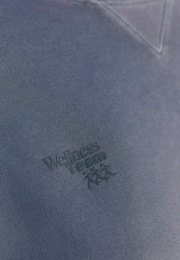 Niebieski bawełniany sweatshirt z teksturowanym logo "Zespół Wellness" w ciemniejszym odcieniu, umieszczonym na lewej piersi.