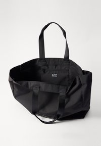 Czarna torba na ramię wykonana z mocnego materiału, z podwójnymi uchwytami, przestronnym wnętrzem i wewnętrzną kieszenią. Posiada naszywkę z logo z przodu.