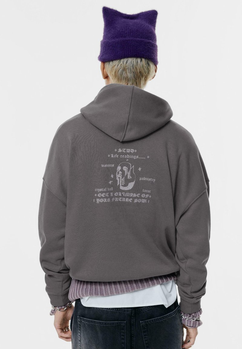 Felpa grigia con cappuccio, caratterizzata da dettagliate grafiche bianche sul retro, polsini a costine e un look stratificato con un orlo striato di viola.