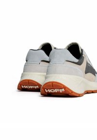 Zapatillas deportivas en gris y beige, hechas de materiales de ante y malla, con una entresuela blanca texturizada y una suela de goma naranja. Logo "HOFF" exhibido.