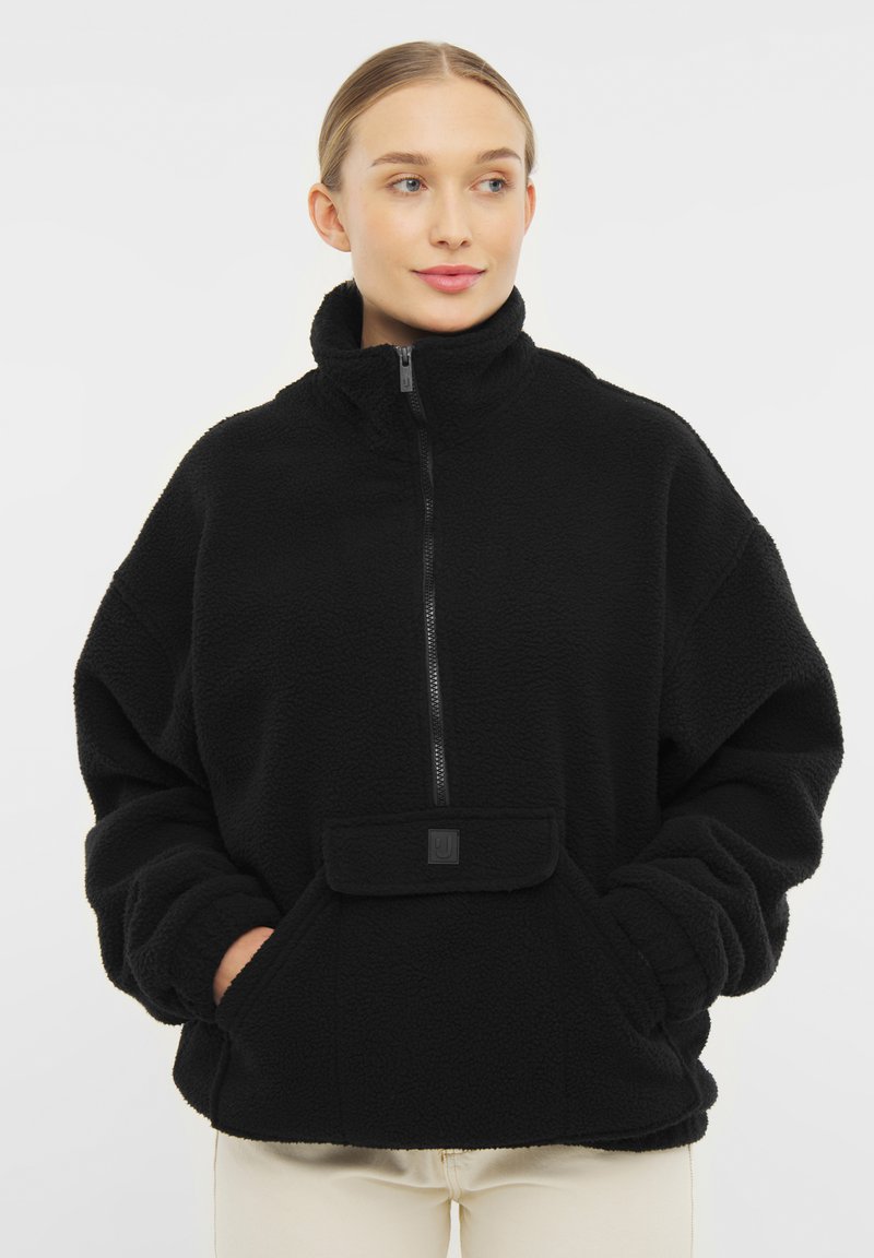 Pullover di pile nero con colletto alto, chiusura a metà zip e tasca frontale. Presenta un esterno morbido e texturizzato e una vestibilità rilassata.