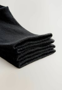 Schwarze Baumwollsocken ordentlich gestapelt, die eine weiche Textur und ein geripptes Design entlang der Öffnungen zeigen. Der Hintergrund ist hell und neutral.