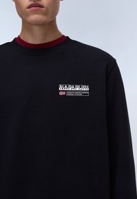 Sort sweatshirt med rund halsudskæring og ribbede manchetter. Viser et logo-patch med tekst og et accent med det norske flag.}}