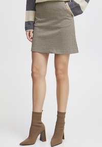 Textured beige mini skirt with a subtle check pattern, paired with brown sock ankle boots featuring a block heel.