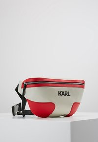 Riñonera de cuero crema y roja, con cremallera negra y correa ajustable. Presenta el logo "KARL" de manera destacada en la parte frontal.