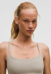 Top ajustado de color beige claro con tirantes finos y escote cuadrado. Textura suave y sin costuras con detalles de diseño mínimos.