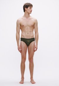 Πράσινα μαγιό σλιπ από λείο, ελαστικό υλικό. Με χαμηλή μέση και ελάχιστη κάλυψη, με καθαρό σχέδιο και χωρίς ορατά μοτίβα.