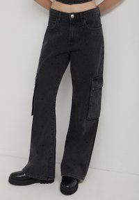 Pantaloni cargo in denim nero con vestibilità ampia, tasche frontali, decorazioni in perline e una tasca laterale sulla gamba sinistra.