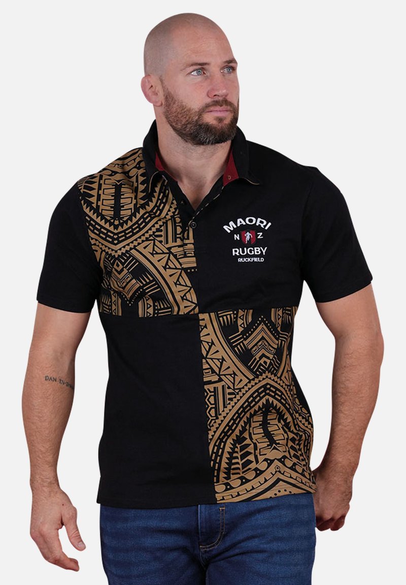 Polo noir avec des motifs inspirés des Māori en or, manches courtes et patte de boutonnage. Présente le logo "MAORI NZ RUGBY RUCKFIELD" sur le devant.