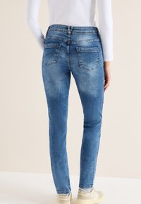 Vaqueros de corte slim en azul claro con un lavado desvaído, con bolsillos traseros y una cinturilla de altura media. Tejido texturizado con un ligero estiramiento.