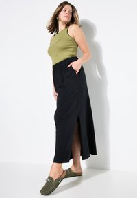Olijfgroene geribbelde tanktop gecombineerd met een zwarte maxi rok met een elastische tailleband en zijsplitsen. Olijfgroene instappers met details.
