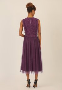 Violetti mekko, jossa on pitsibody, sahalaitaiset reunat ja pörröinen hame, jossa on pilkkuja, yhdistetty mustiin korkokenkiin ja takavetoketjuun.