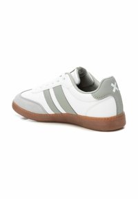 Zapatilla deportiva blanca con acentos grises y tres rayas grises. Presenta una parte superior sintética suave y una suela de goma texturizada.