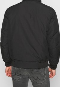 Schwarze Bomberjacke aus glattem Material, mit gerippten Bündchen und Saum. Schlichtes Design ohne auffällige Muster oder Verzierungen.