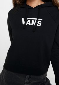 Sudadera negra de tejido suave, con un logo blanco de "VANS". Tiene capucha con cordón y dobladillo acanalado.