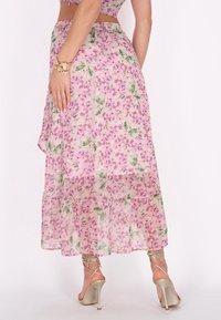 Gonna maxi floreale rosa con una texture trasparente, caratterizzata da un orlo a strati e dettagli verdi. Indossata con scarpe con tacco alto dorate a strisce.