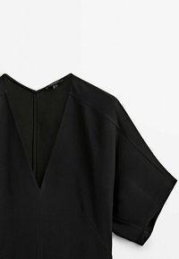 Schwarzes V-Ausschnitt-Top aus glattem Stoff mit kurzen Ärmeln, das über ein dezentes Nahtdetail und einen Rückenverschluss verfügt.