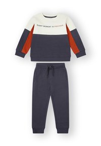 Sudadera azul marino y crema con detalles en naranja, con el texto "CADA MOMENTO ES PRECIOSO." Combinada con pantalones de chándal azul marino a juego. Mezcla suave de algodón.