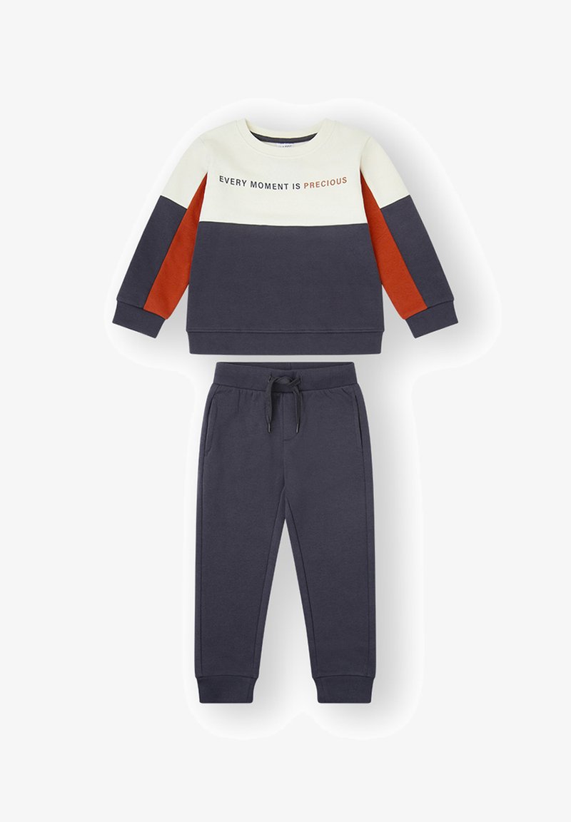 Sudadera azul marino y crema con detalles en naranja, con el texto "CADA MOMENTO ES PRECIOSO." Combinada con pantalones de chándal azul marino a juego. Mezcla suave de algodón.