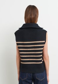 Ärmlös stickad tröja i mörk marinblå med horisontella beiga ränder på baksidan och en bred krage. Texturen är jämn med en figursydd silhuett.