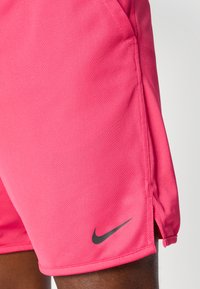 Vaaleanpunaiset Nike-shortsit, jotka on valmistettu teksturoituneesta kankaasta. Shortsien vasemmassa alakulmassa on musta logo, ja sivuilla on liikkumista helpottavat halkiot.