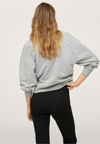 Oversized grijze trui met aflopende schouders en lange mouwen, gecombineerd met zwarte strakke broek. Zachte textuur, casual ontwerp.