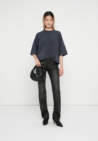 Un pulover tricotat supradimensionat de culoare albastru închis, blugi negri slim cu un luciu ușor și o geantă de umăr din piele neagră. Ținuta are un design minimalist.