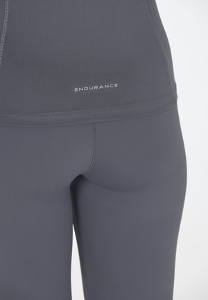 Graue sportliche Leggings mit einer glatten Oberfläche, die ein Logo trägt, das "ENDURANCE" in der Nähe der Taille zeigt. Das Material ist eng anliegend.