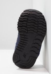 Černá gumová podrážka boty s hlubokým vzorem běhounu, texturovaným povrchem a modrým látkovým svrškem připevněným u paty.