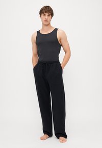 Schwarzes Tanktop und locker sitzende Hose aus weichem Stoff. Die Hose verfügt über einen Kordelzug und Taschen, die für Komfort und Bewegungsfreiheit konzipiert sind.