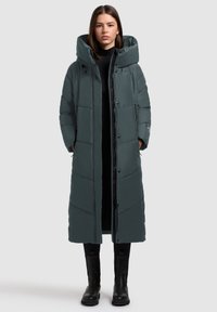 Duga pufasta jakna tamnosive boje, s visokim ovratnikom, zatvaranjem na zip i kopčom, lijepim prošivom i bočnim džepovima. Glatka, vodootporna tkanina.