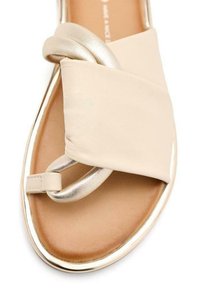 Sandalo beige con tomaia in tessuto liscio e imbottito. Presenta un dettaglio ad anello in oro metallico e un bordo argentato lucido lungo la suola.
