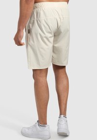Pantalones cortos deportivos color crema con cintura elástica. Tela suave y ligera con bolsillos laterales. Combinados con zapatillas blancas.